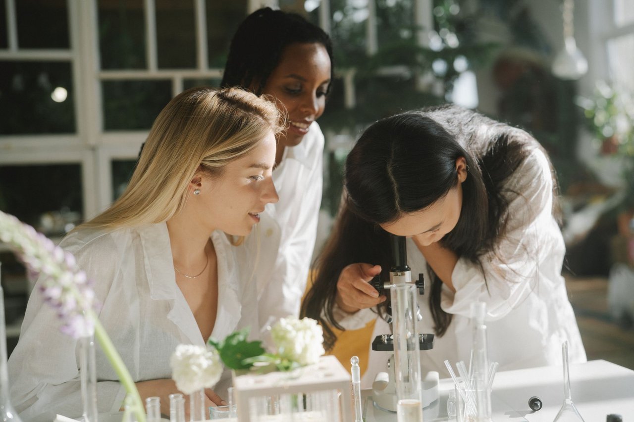 Três jovens cientistas trabalham juntas em um laboratório iluminado.