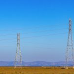 Torres e linhas de transmissão de energia elétrica em uma paisagem natural sob céu azul.
