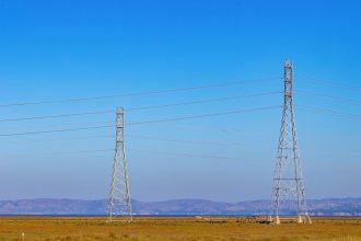 Torres e linhas de transmissão de energia elétrica em uma paisagem natural sob céu azul.