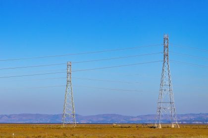 Torres e linhas de transmissão de energia elétrica em uma paisagem natural sob céu azul.