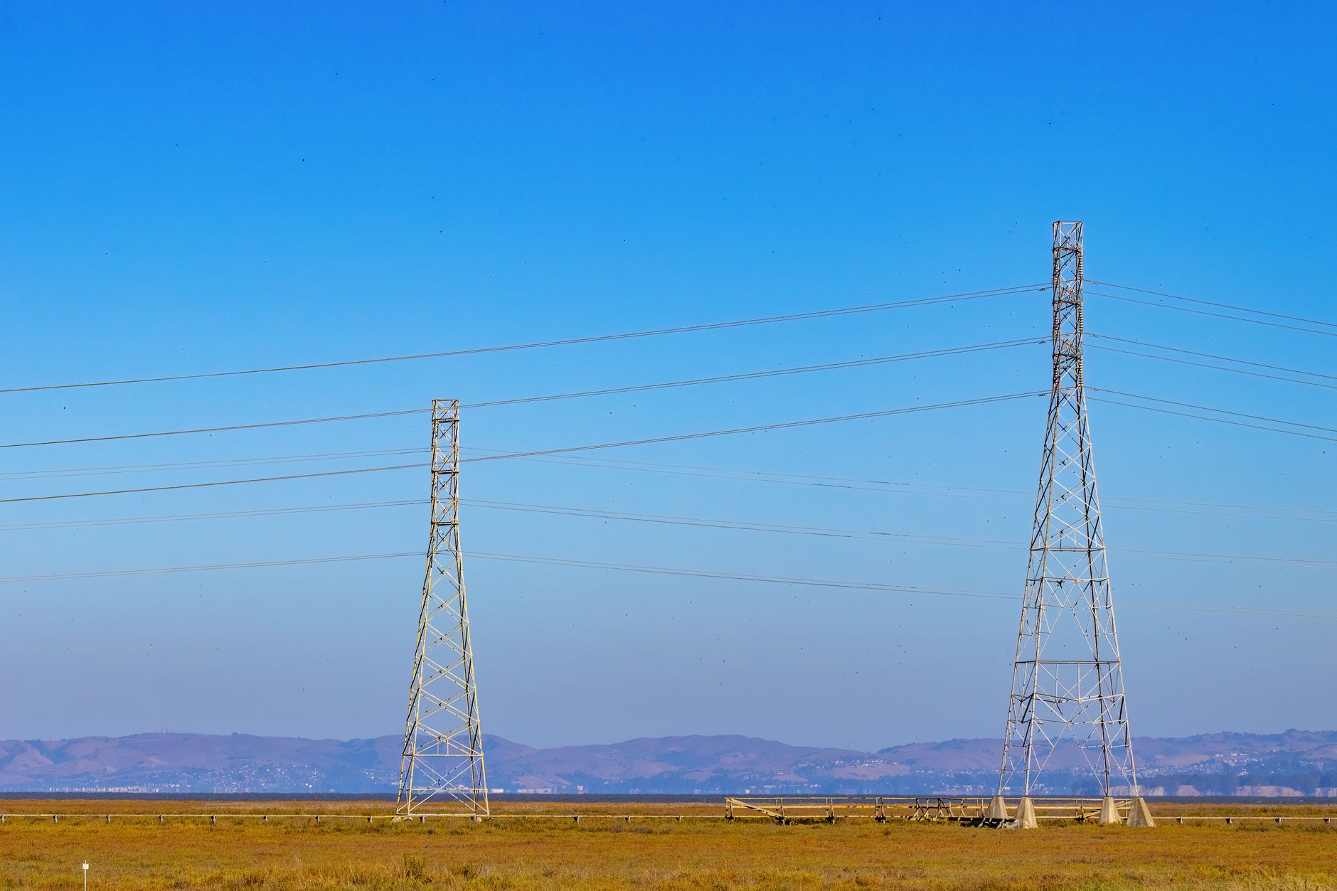 Torres e linhas de transmissão de energia elétrica em uma paisagem natural sob céu azul.